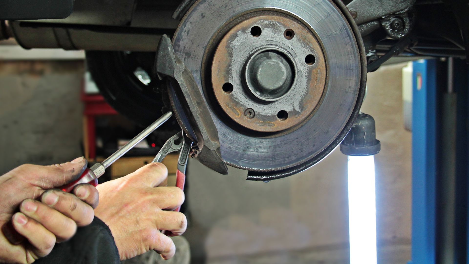 Mechanic repairing car brake disc with pliers in auto repair shop