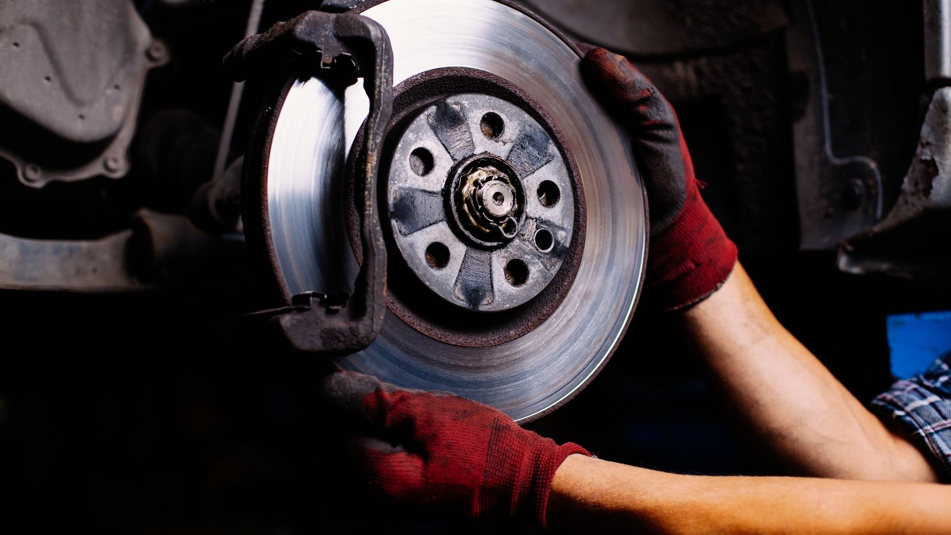 Mechanic repairing car brake disc with red gloved hands
