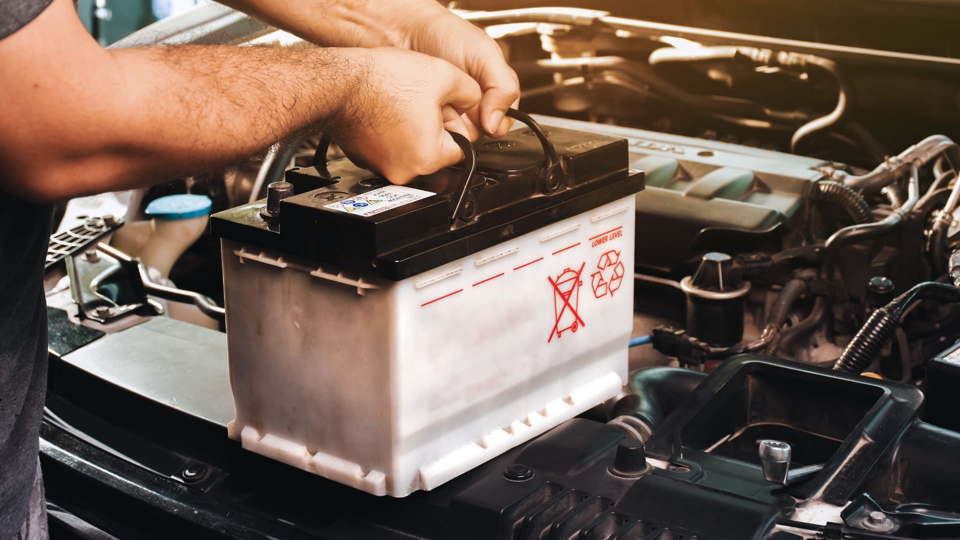 Hand installing car battery in engine compartment with recycling symbol